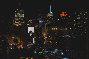 The reflection of a couple kissing in a window the the NYC skyline out the window.