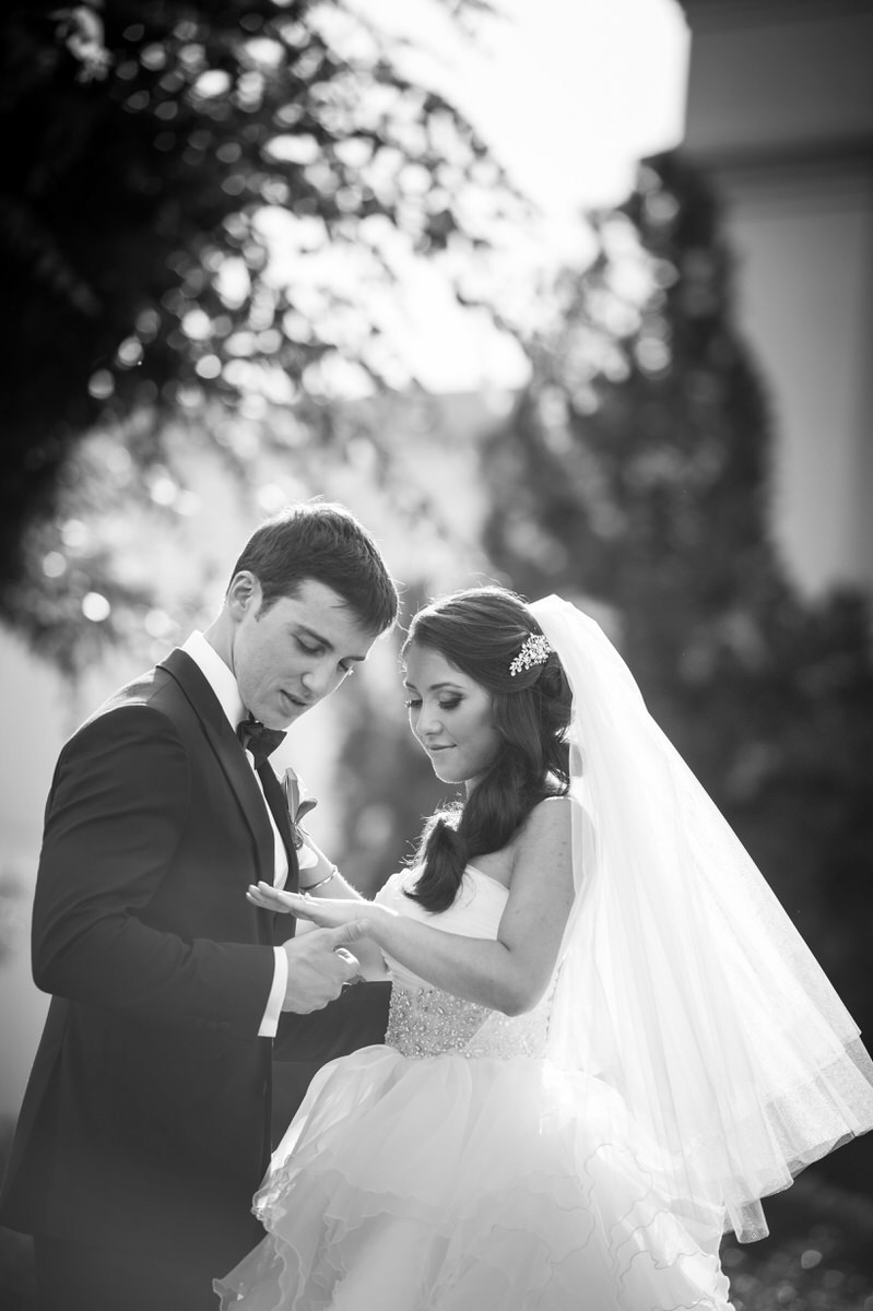 A bride standing next to a groom as they both look down at the ring on her finger. 