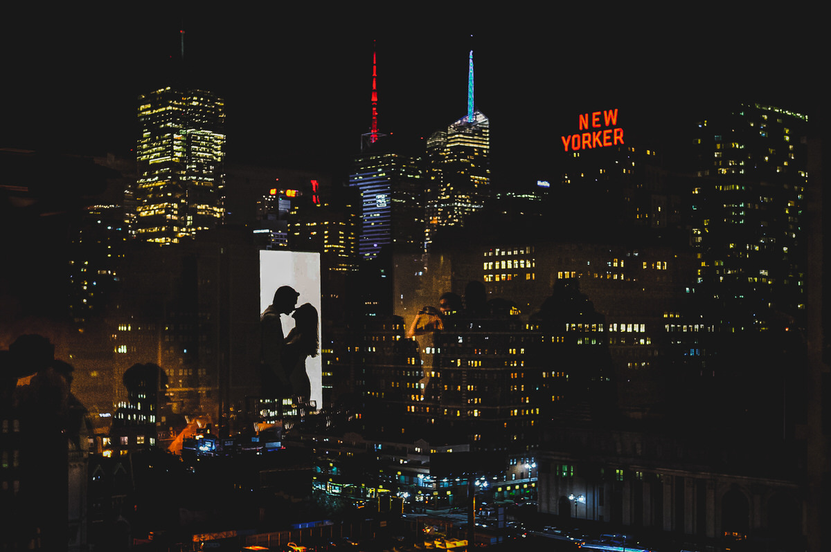 The reflection of a couple kissing in a window the the NYC skyline out the window. 