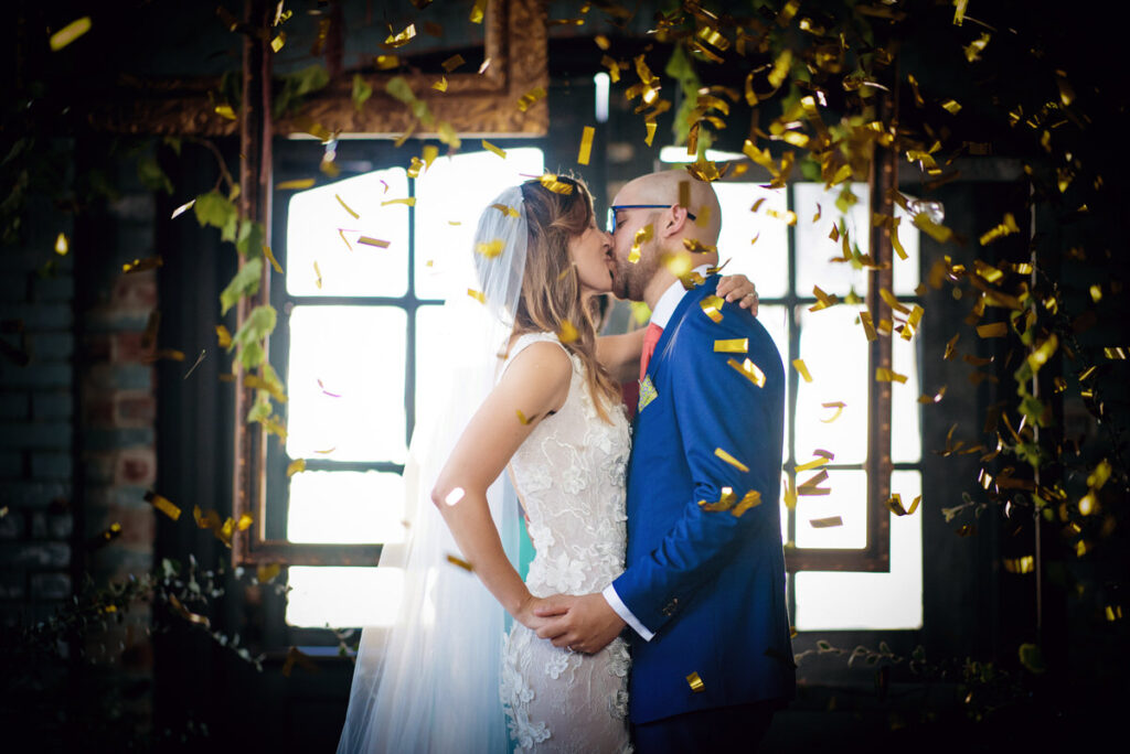 A bride and groom kissing as confetti falls around them.