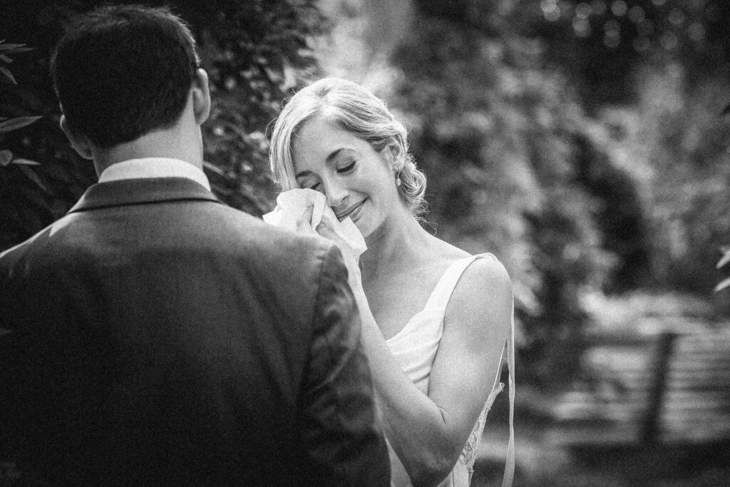 A bride wiping away tears as she stands in front of a groom.