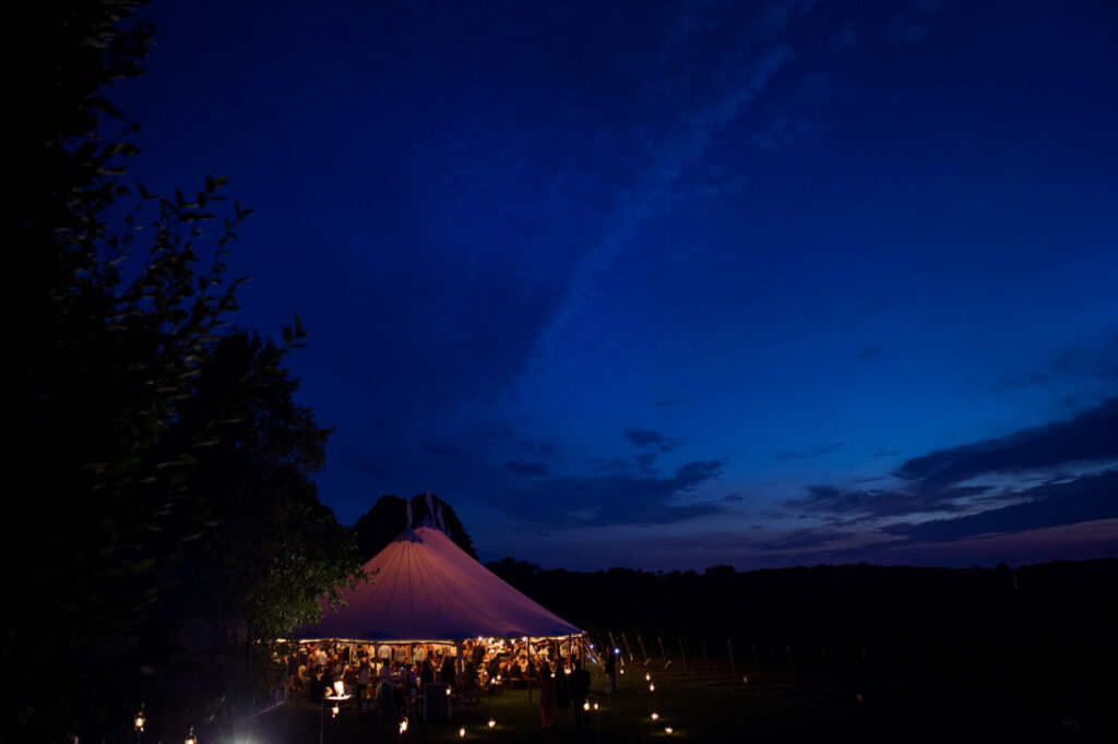 A large white tent for a wedding reception lit up against the dusk sky.