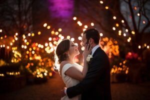 A bride and groom embracing in front of a lit up tree