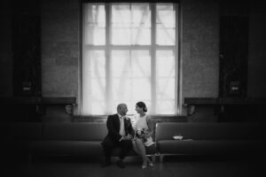 A bride and groom sitting on a couch in front of a window, capturing the essence of their intimate NYC elopement.