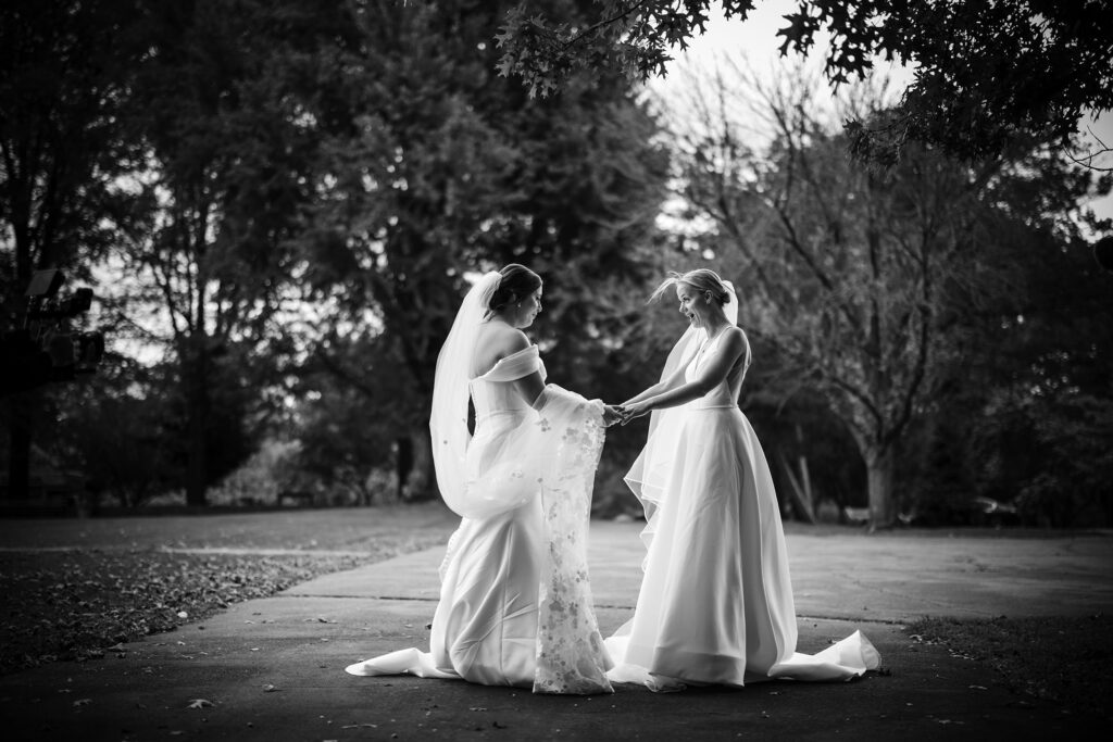Two brides sharing their first look on their wedding day, standing next to each other in a park.