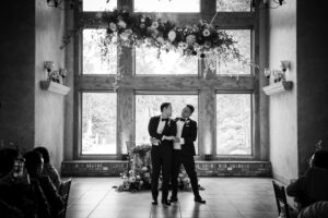 A black and white photo capturing a graceful wedding first dance with two grooms.