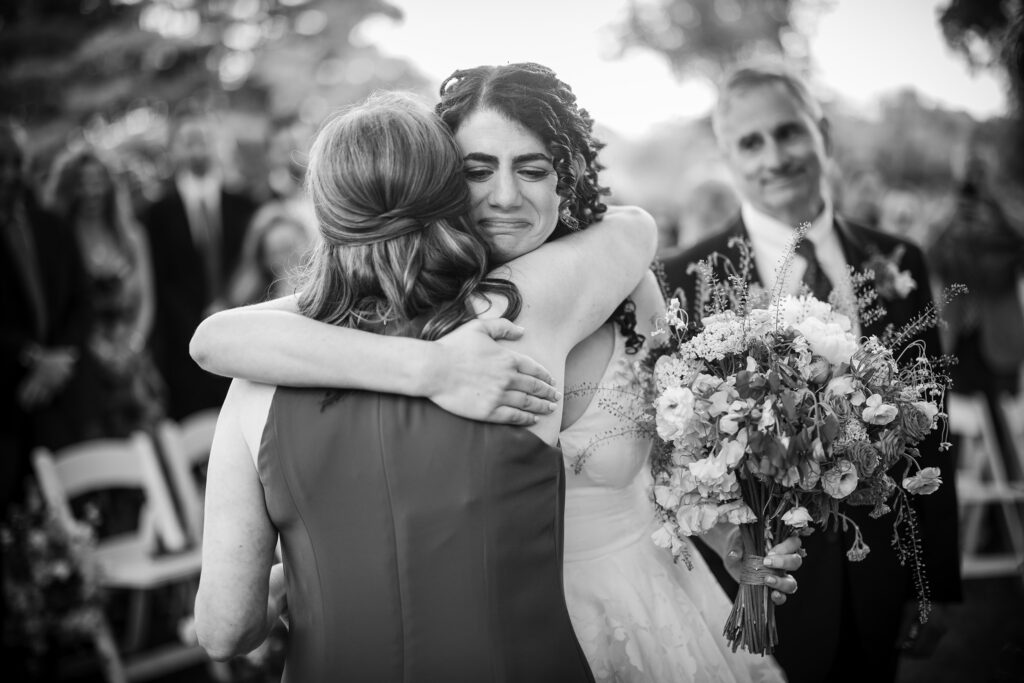 A bride hugging her mother during a wedding ceremony, captured in a heartfelt documentary moment.