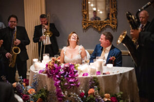 A photojournalism shot capturing a bride and groom at a table with musicians.