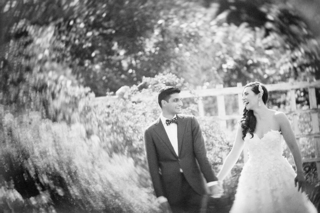 A black and white photo of a bride and groom walking through the Brooklyn Botanic Garden at their wedding.