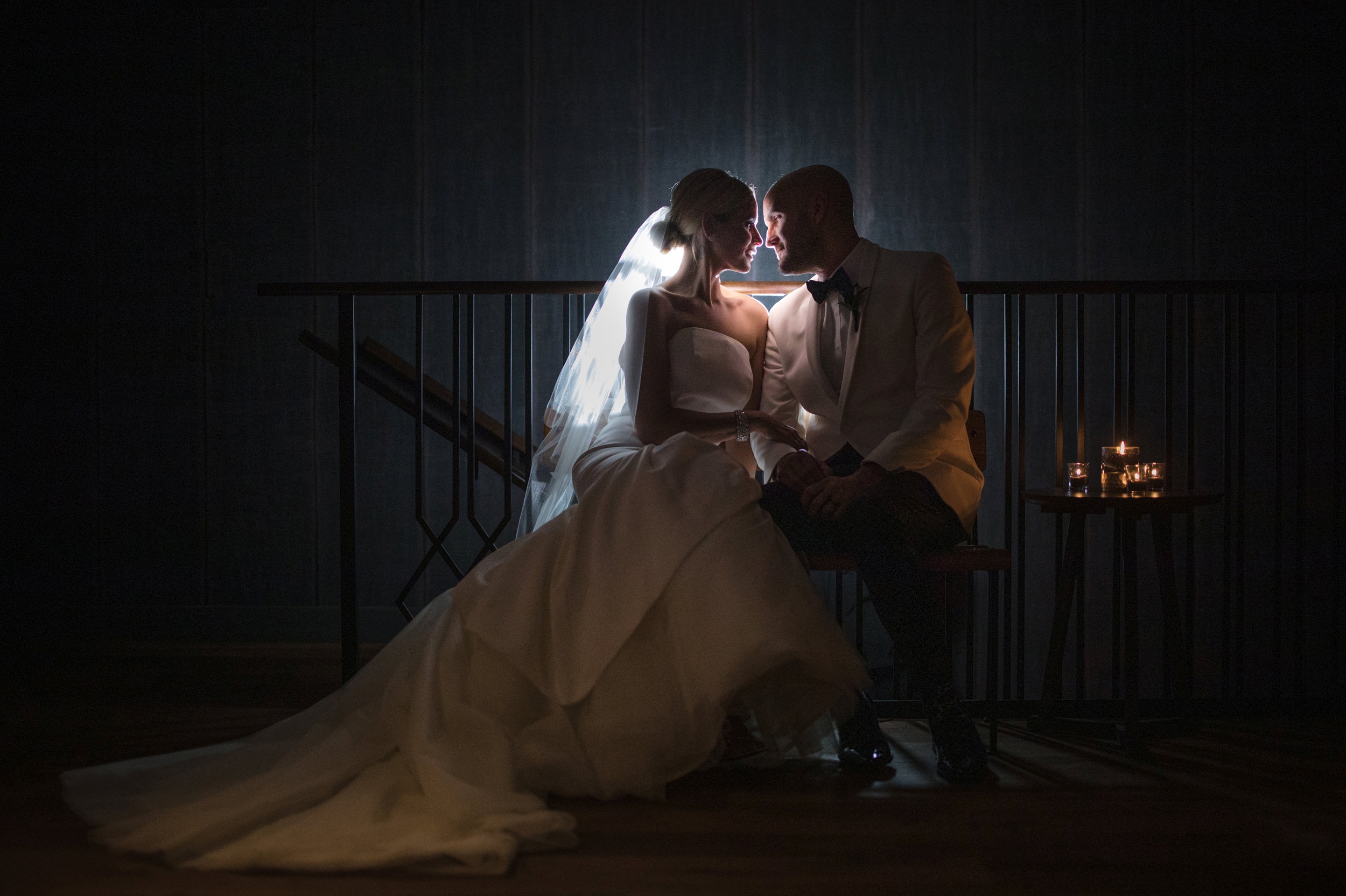 A bride and groom, amidst the romantic ambiance of the Fitler Club, sit together on a staircase in the dark during their enchanting wedding day.