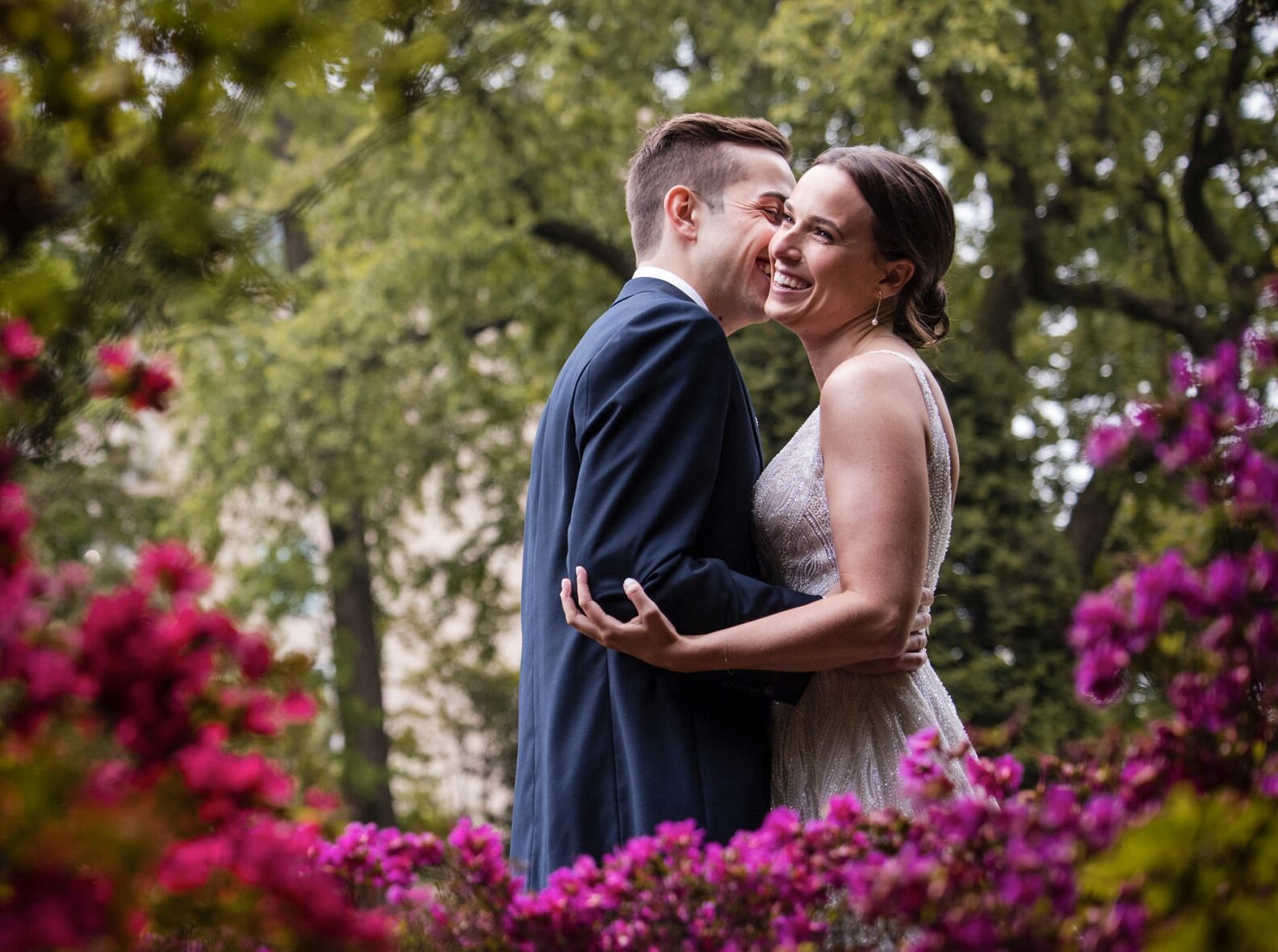 A bride and groom embrace in front of flowers at their Brooklyn Botanic Garden wedding.