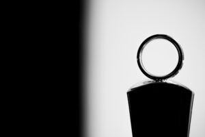 A black and white photograph of a bottle with a wedding ring on it.