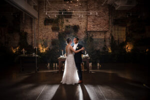 A bride and groom sharing their first dance in front of a light in a dark room at their wedding.
