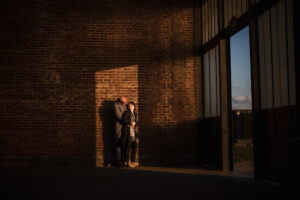 An engaged couple standing in front of a brick wall.