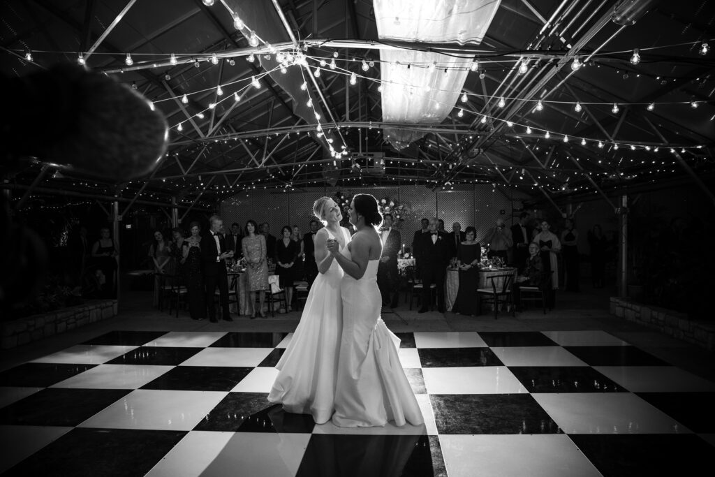 Two brides gracefully performing their first dance on a checkered floor at their wedding.