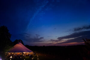 A bedell cellars wedding tent lit up at dusk in a field.