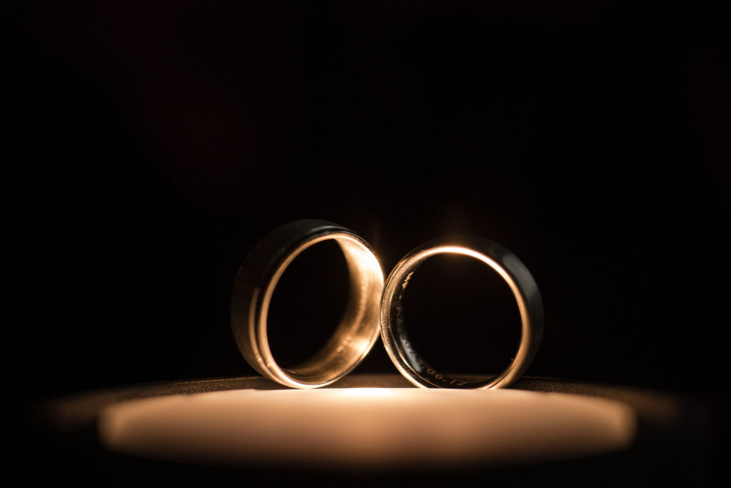 Two wedding rings delicately placed on top of a flickering candle at rehearsal dinner, symbolizing the eternal union and evolution of love.