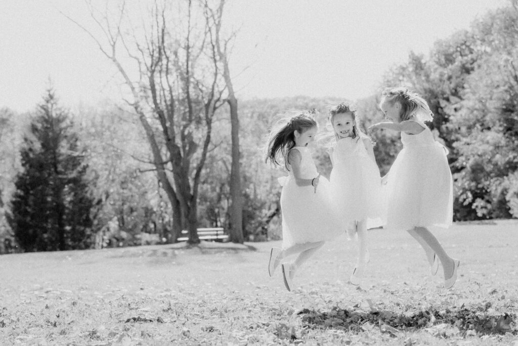 A black and white photo of three flower girls jumping in the air at a Sands Point Preserve wedding.