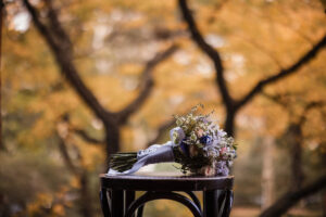 A wedding bouquet sits on a chair in front of trees.