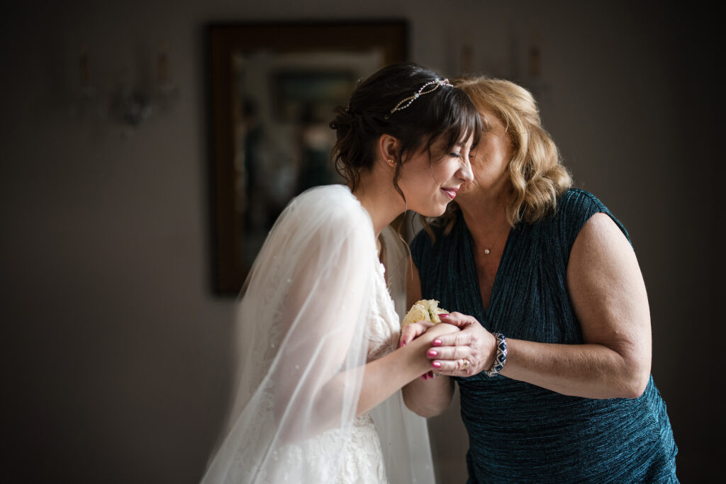 A bride and her mother sharing a heartfelt moment in front of a mirror on their wedding day.