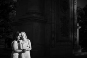A black and white photo of two engaged women in front of a monument.