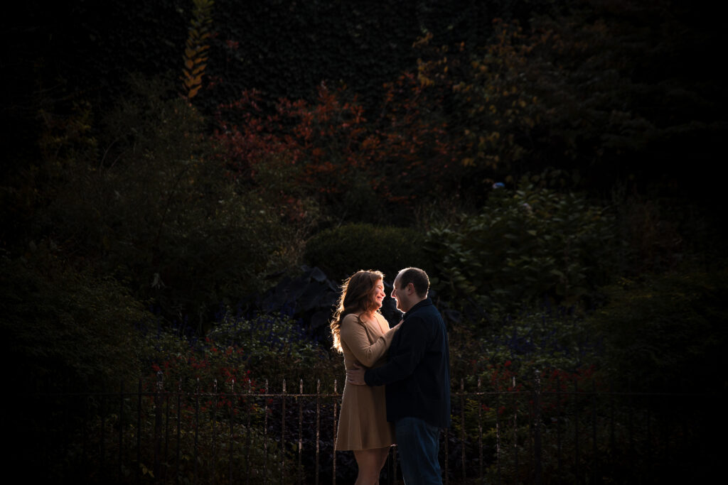An engaged couple standing in the dark in a garden during their engagement session by a New York engagement photographer.