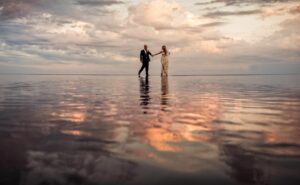 A destination wedding bride and groom standing in the water at sunset.