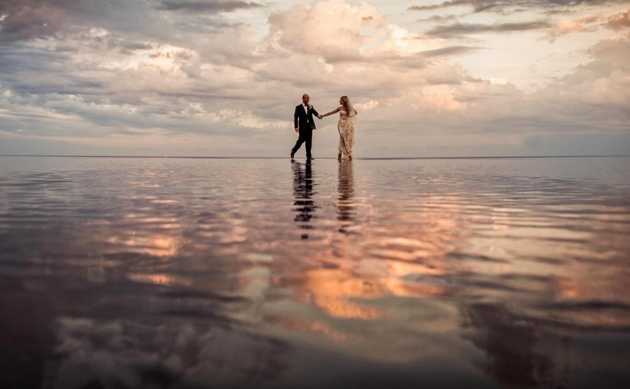 A destination wedding bride and groom standing in the water at sunset.