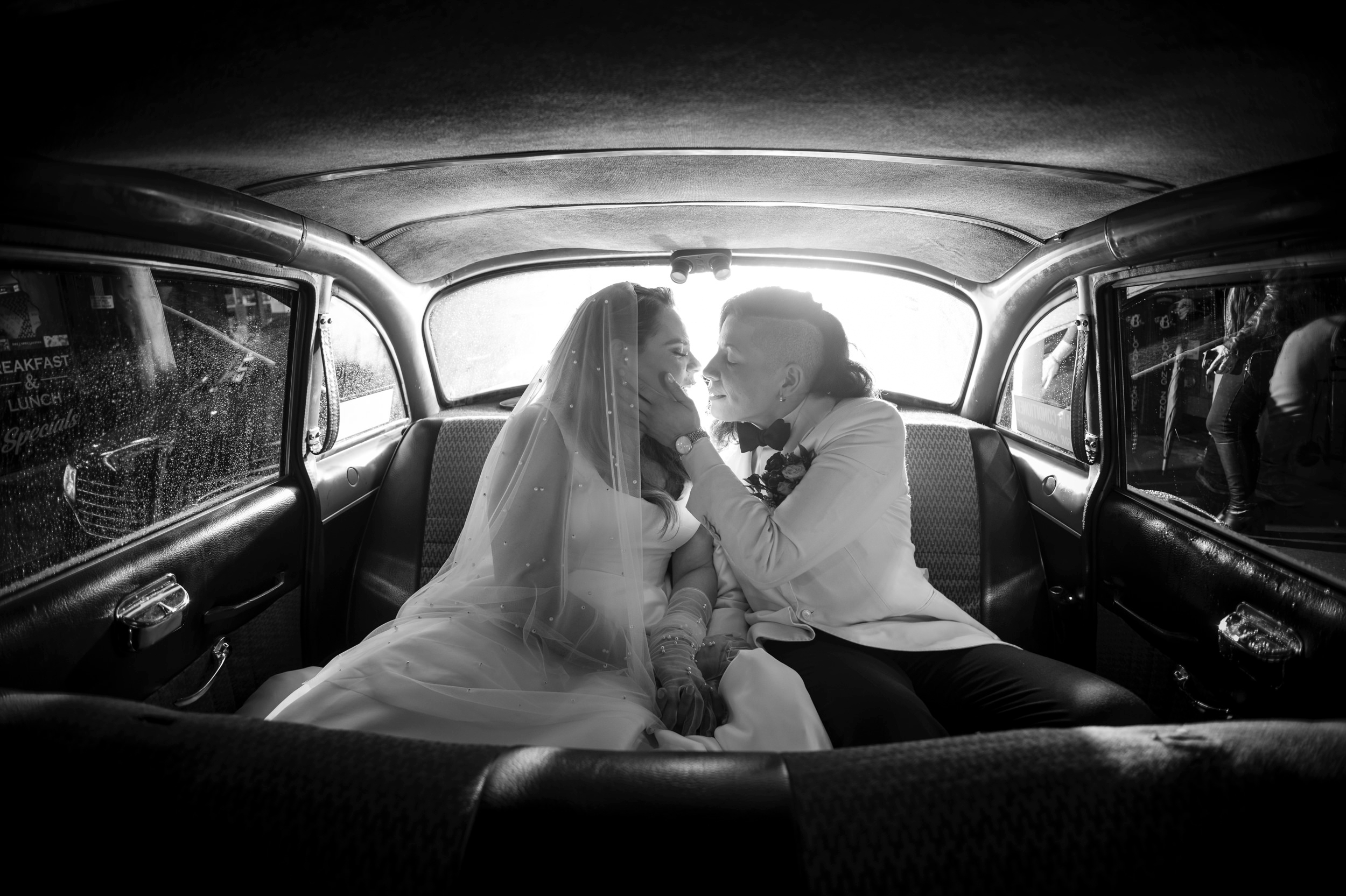 Two brides kiss in the back seat of a vintage NYC cab at their wedding.