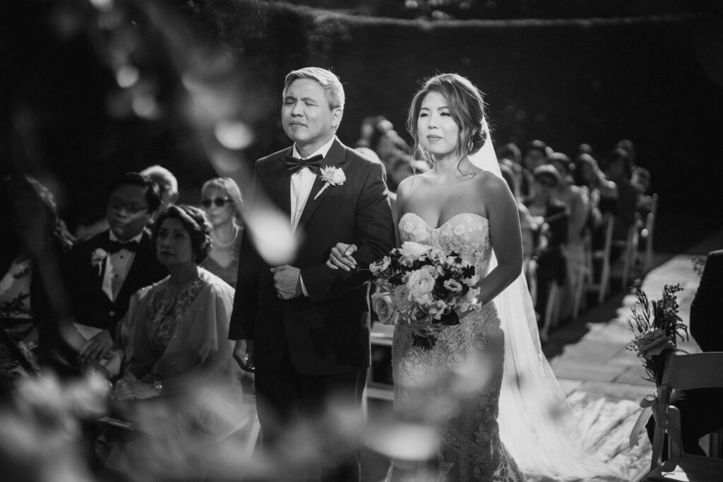 A black and white photo of a bride and groom walking down the aisle during an outdoor wedding ceremony.