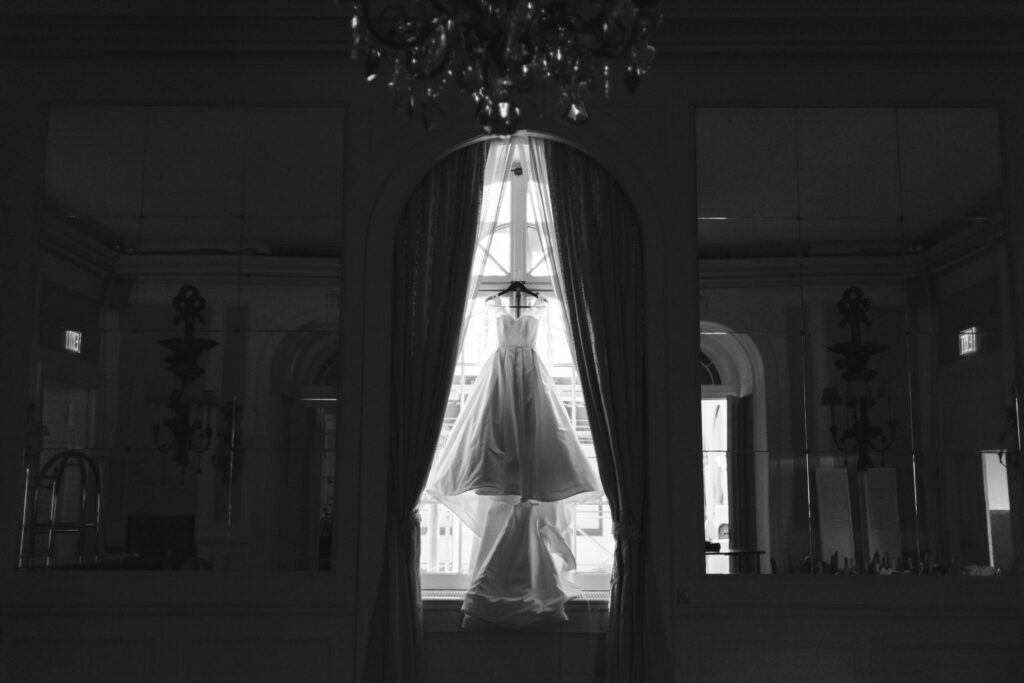 A black and white photo of a wedding dress hanging in a window at Colony Club, NYC.