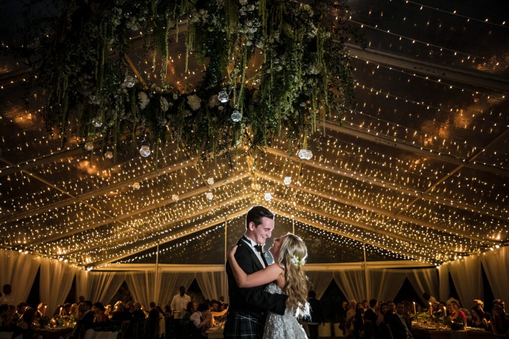 In a beautiful destination wedding, the bride and groom share their first dance in a tent under enchanting string lights.