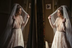 A bride is putting on her wedding veil in front of a mirror at the Lyndhurst Mansion wedding venue.