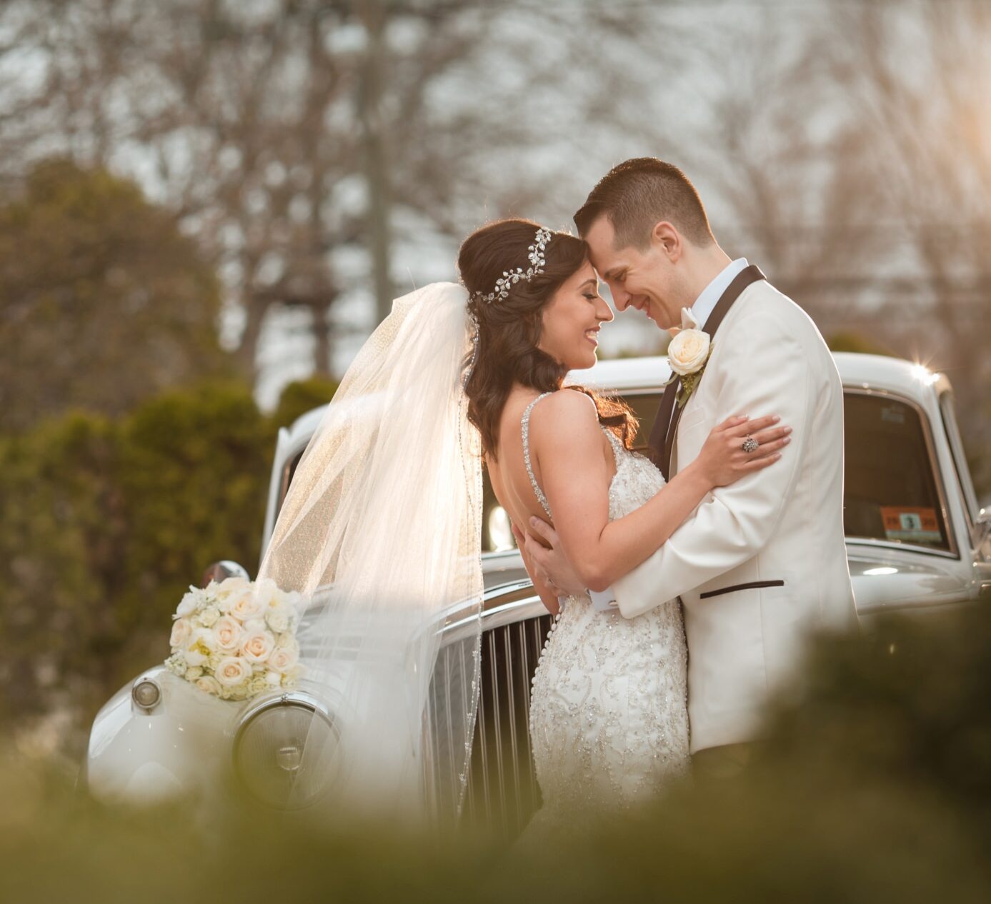 A bride and groom share a romantic kiss beside a classic car at their Estate at Florentine Gardens wedding.