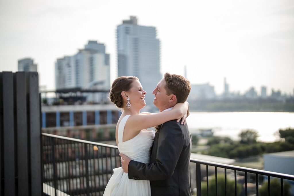 A bride and groom embrace on a balcony at the Wythe Hotel, overlooking the city.