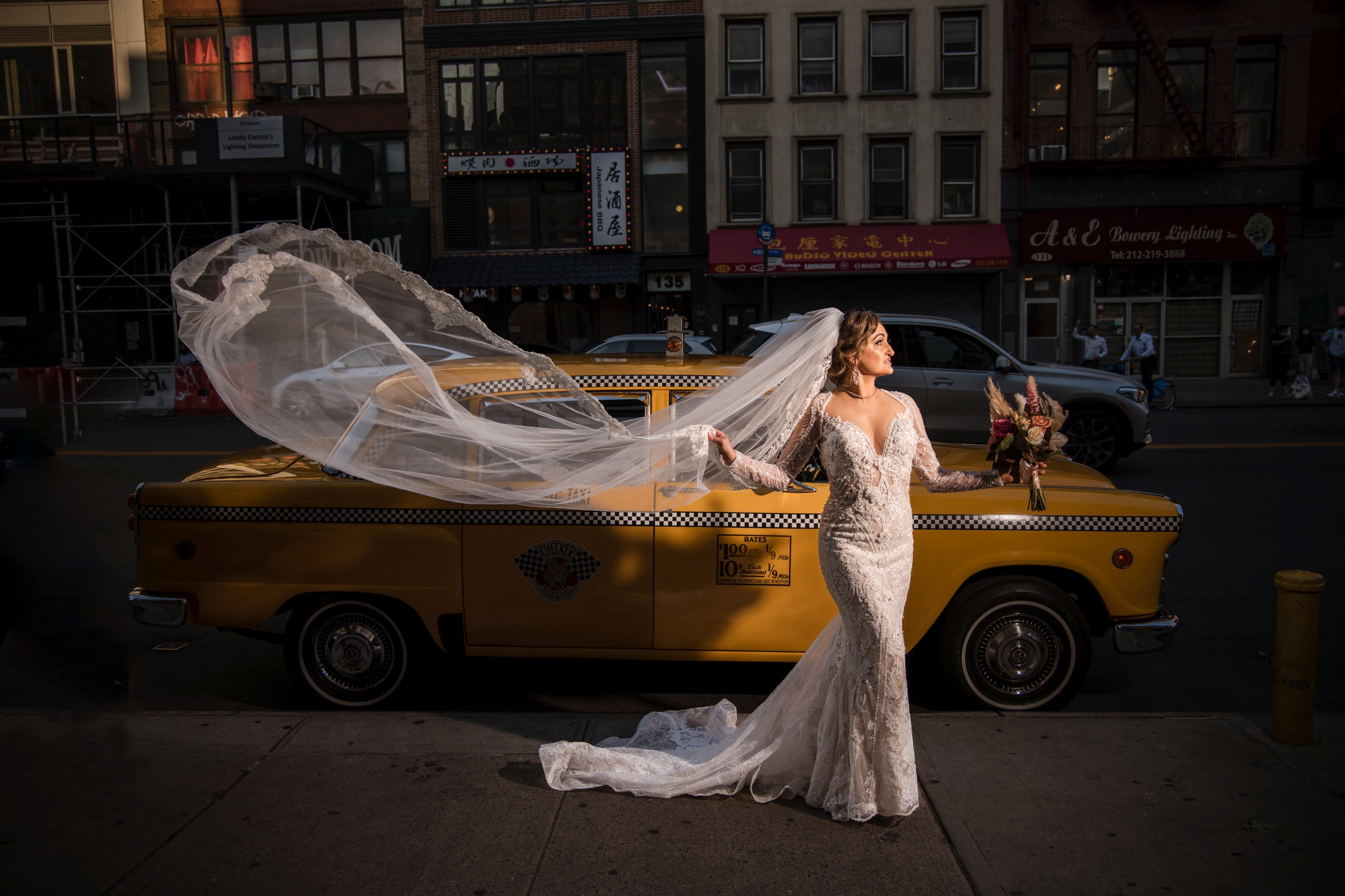 A Capitale bride poses in front of a yellow taxi.