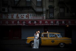 A wedding couple poses in front of a vintage NYC cab.