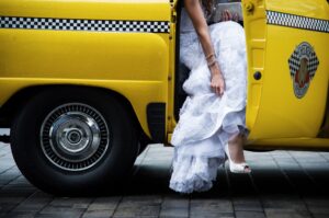 A woman in a wedding dress sitting in the back of a vintage yellow taxi.