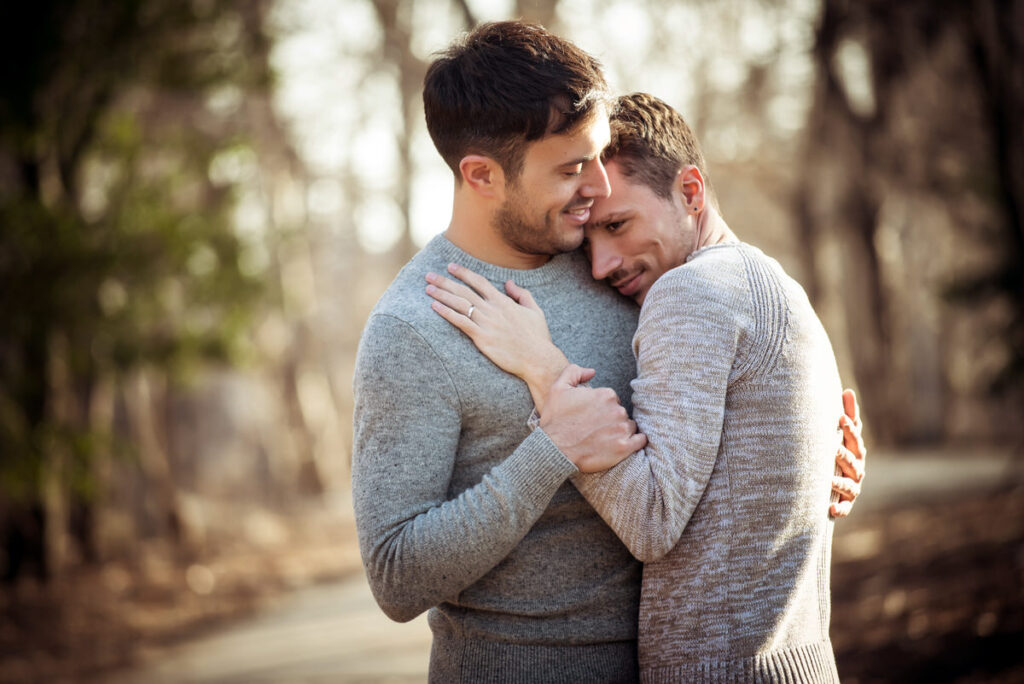 An intimate moment between a couple hugging in a serene wooded area, combining casual and formal elements in their engagement outfits