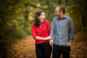 "A couple playfully walking along a leaf-strewn forest path, exemplifying a blend of casual and formal engagement attire."