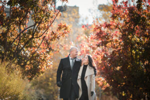 A couple walking hand in hand among vibrant fall foliage, with their engagement outfits thoughtfully chosen to match the season