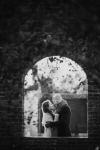 A monochrome image of a couple in a loving embrace within a brick archway, conveying a timeless and romantic feel.