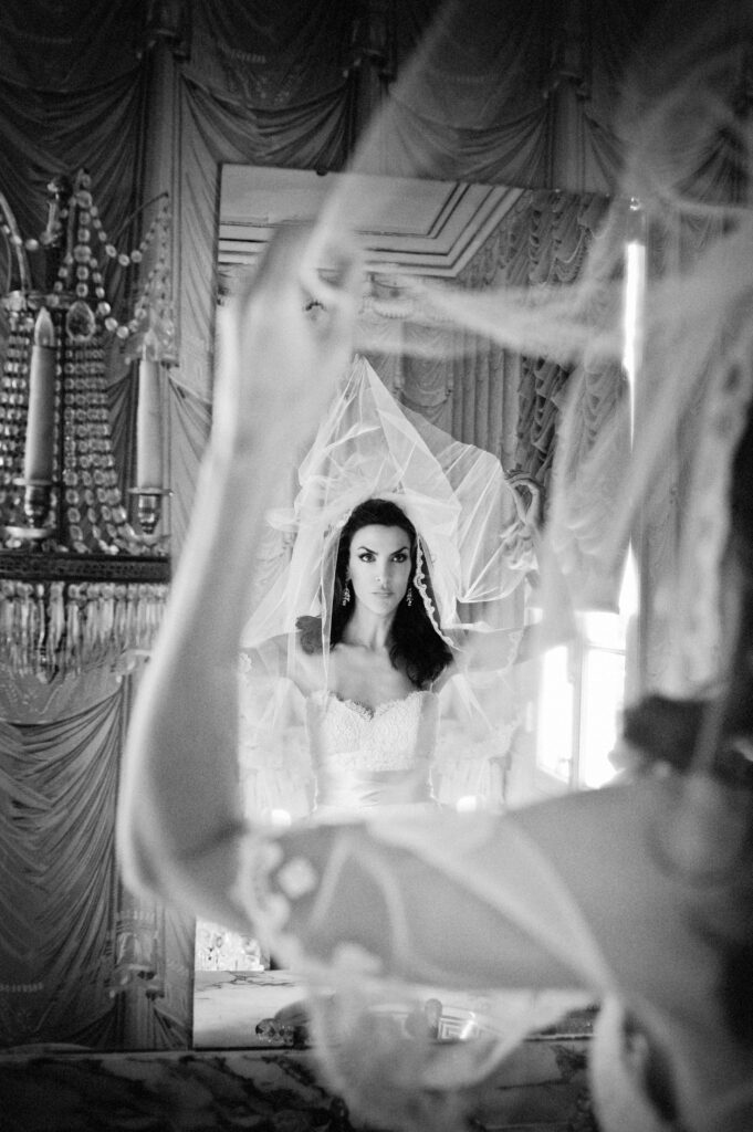 A bride preparing for her New Orleans destination wedding, putting on her veil in front of a mirror.
