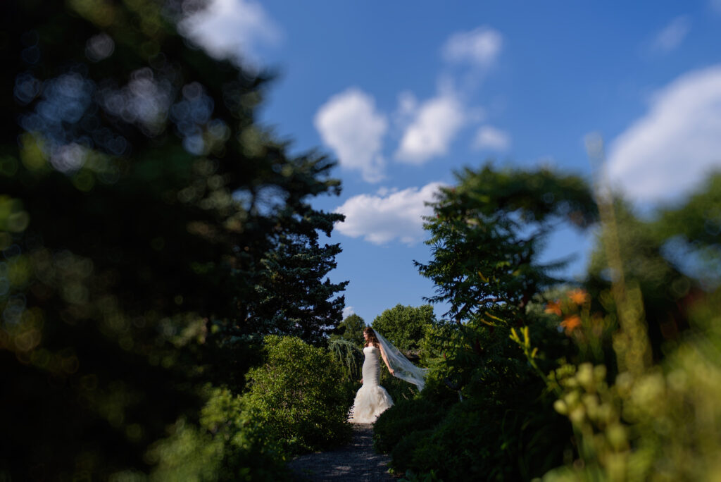 A bride is walking down a path in the woods at her Wave Hill wedding.