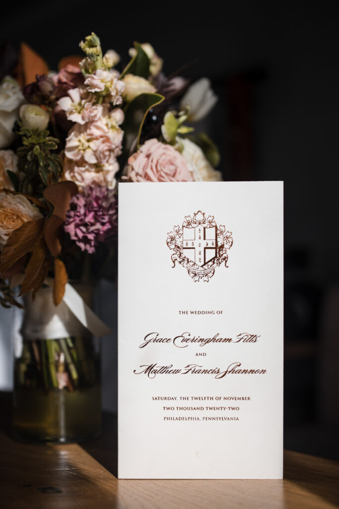 A wedding invitation sitting on a table next to a vase of flowers.