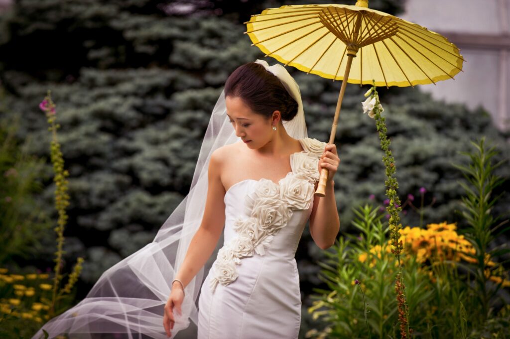 A woman in a white dress holding a yellow umbrella at a Wave Hill wedding.