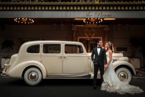A bride and groom pose in front of a vintage car at their wedding at The Pierre.