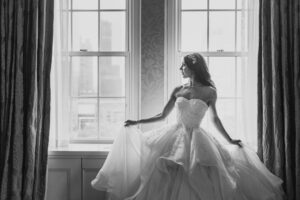 A bride in a wedding dress is standing in front of a window at The Pierre.
