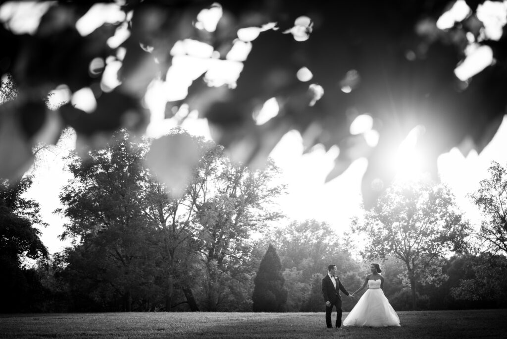 bride and groom walking through a sunlit field with leaves