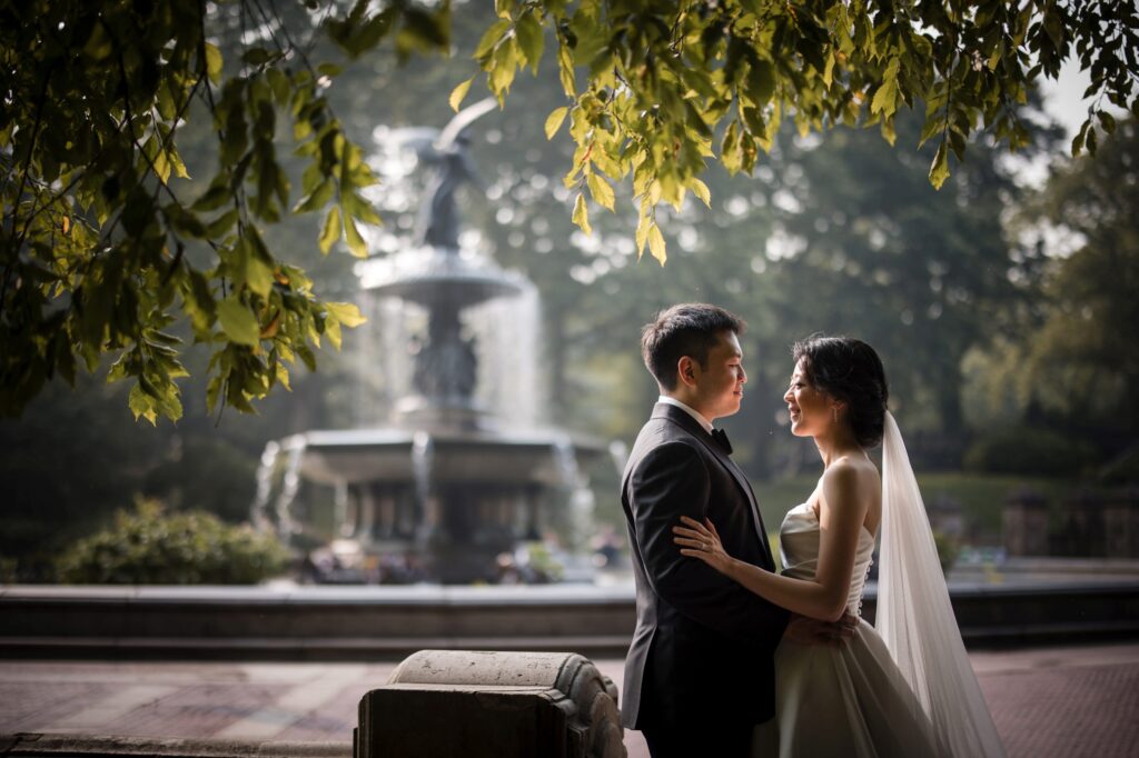 A newlywed couple sharing an intimate moment by a fountain in Central Park during their wedding photoshoot.